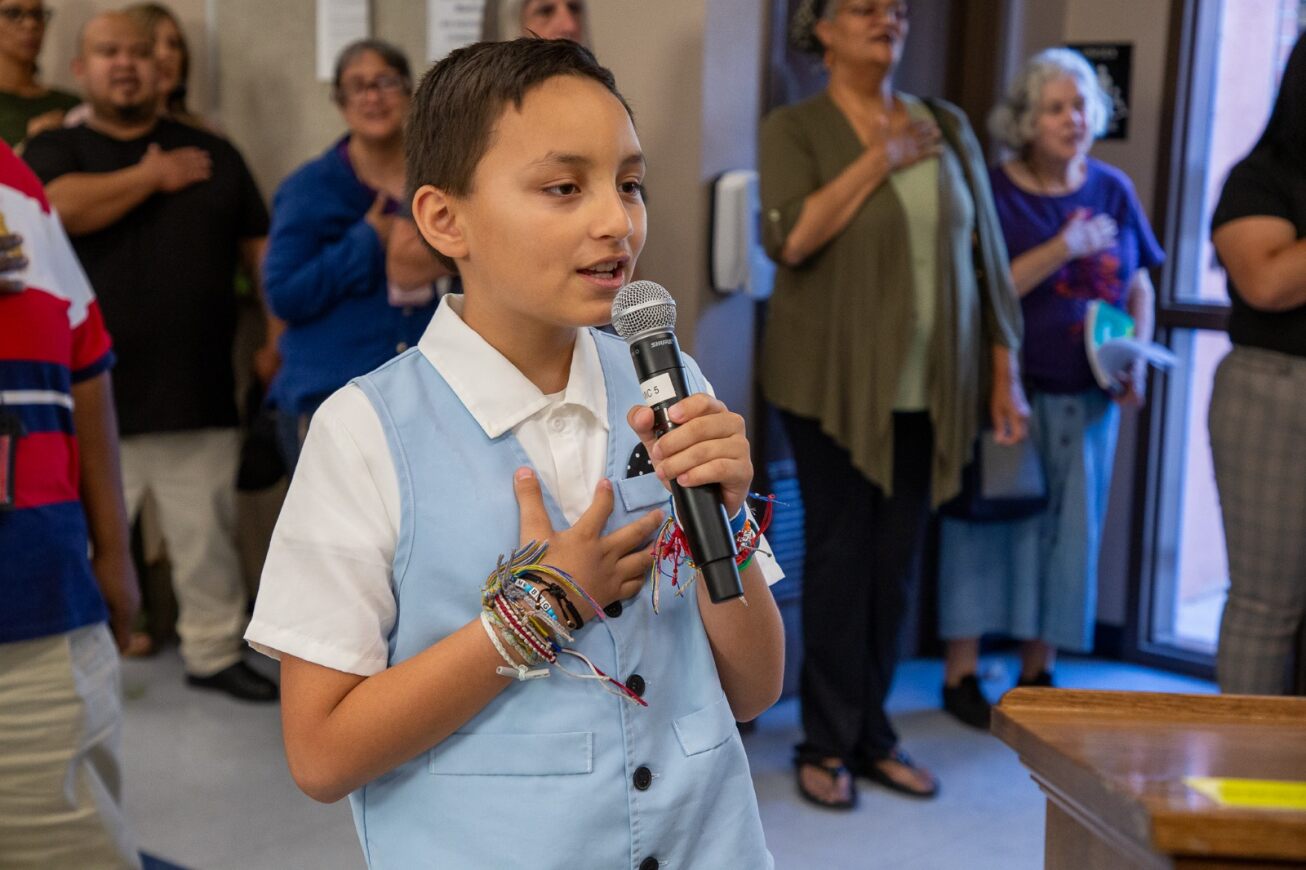 A young boy in a blue vest gives the Pledge of Allegiance at the Governing Board meeting
