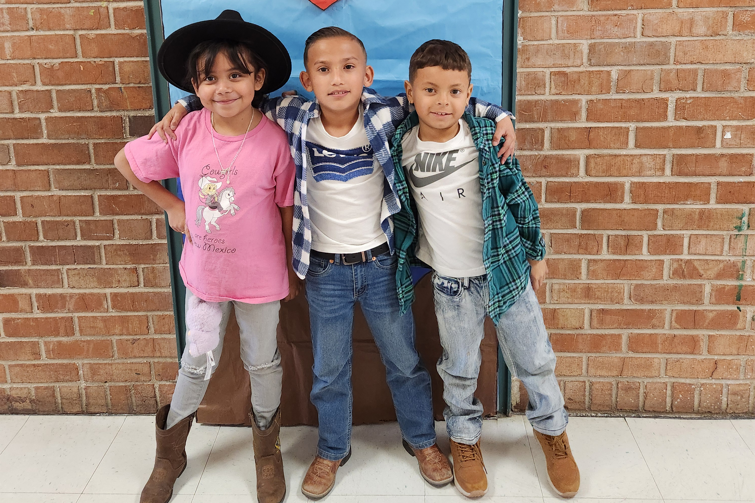 A little girl and two little boys pose for a photo to show off their western wear