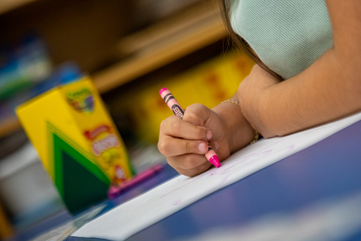 Closeup of a girl's hand coloring with a pink crayon