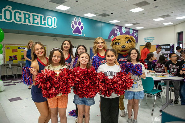 A group of girls pose with red pom poms with UofA cheerleaders and Wilma, the Wildcat mascot