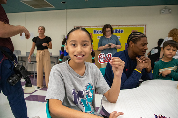 A girl smiles as she holds up a Cats sticker