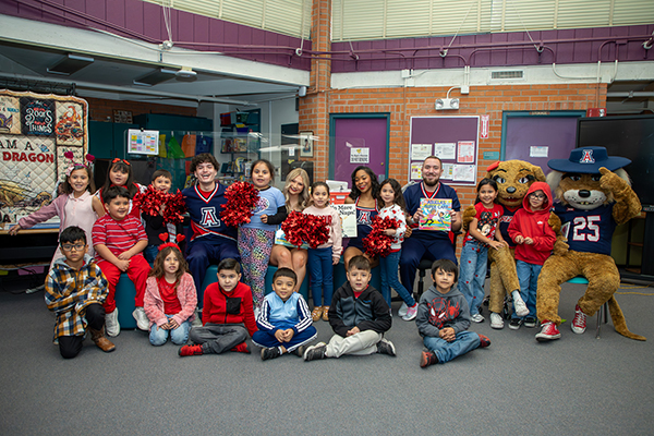 Four UofA cheerleaders, Wilma and Wilbur and a group of students pose for a photo in the library