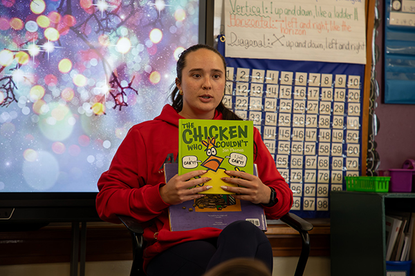 A woman in a red hoodie holds up a book called The Chicken Who Couldn't