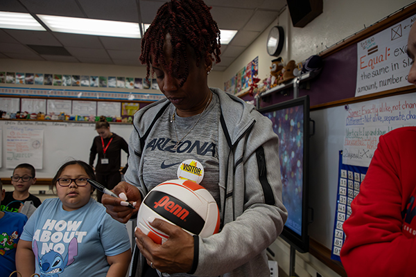 A woman in a gray hoodie signs a volleyball