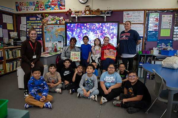 The two guest readers pose with a classroom of students and their teachers