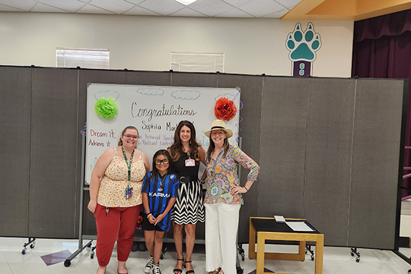 A girl wearing glasses, second from left, with three women stand in front of a whiteboard celebrating her win