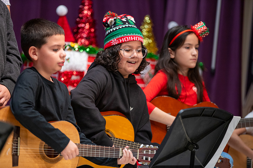 Three students play guitar in front of a holiday backdrop