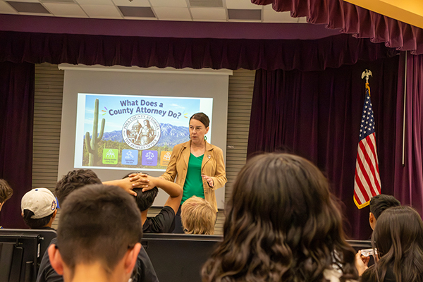 A woman talks to students as she stands in front of a presentation screen about what a county attorney does