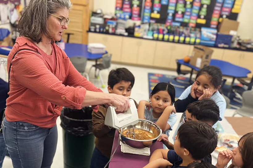 A woman shows a group of students how to blend pumpkin in a mixing bowl