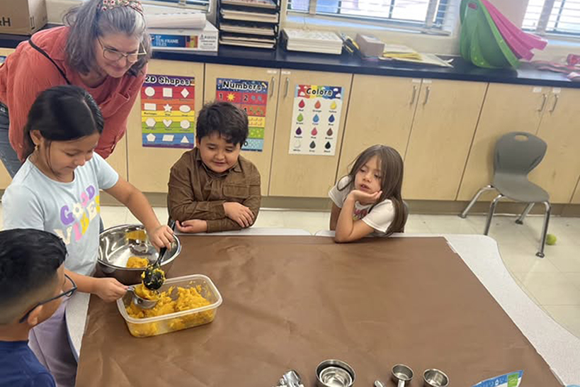A woman observes as a girl scoops pumpkin into a bowl