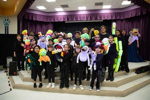A group of students and their puppets pose on stage