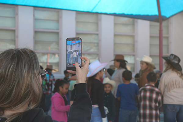 A mom holds up her phone to capture video of the students square dancing