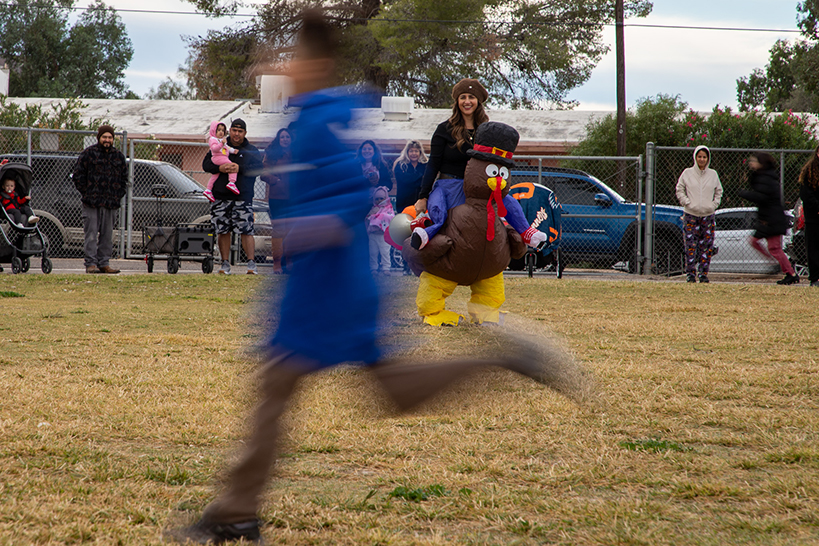 A boy runs by in a blur, while a woman in an inflatable turkey costume watches in the background