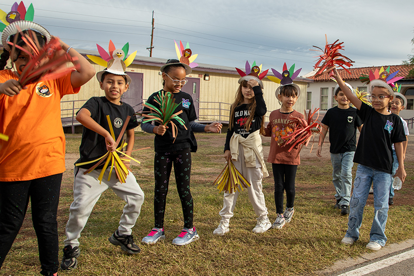 Students wearing paper turkey headbands wave paper pompoms