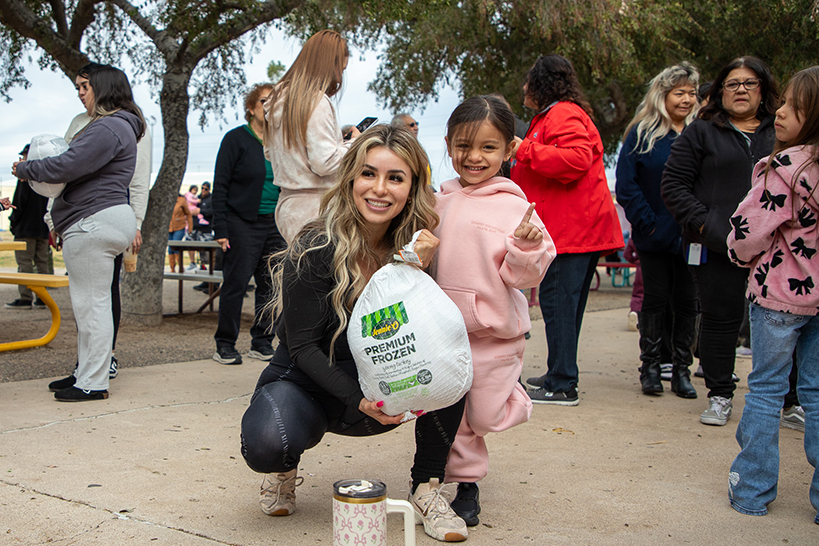 A woman kneels holding a frozen turkey next to a little girl holding up one finger