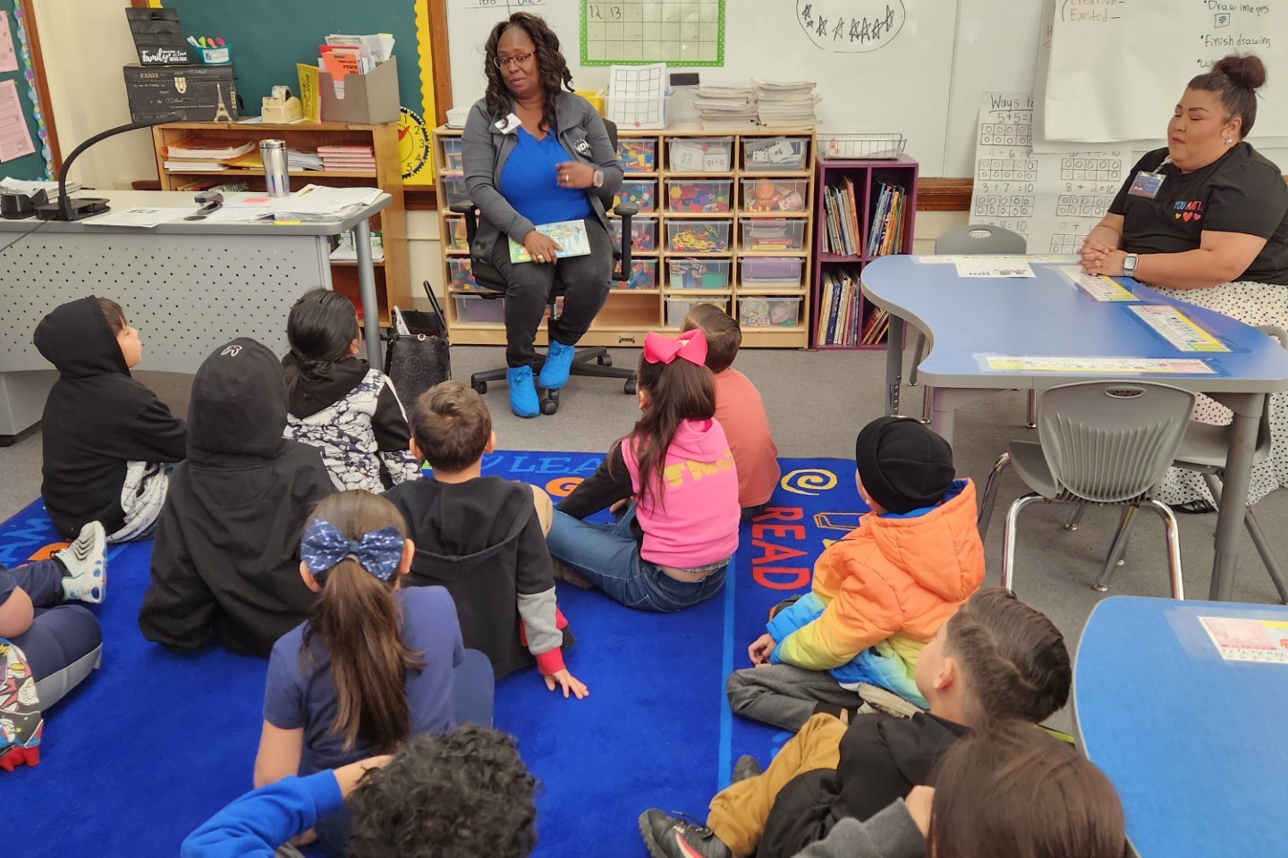 A guest reader shares a story with students sitting on the floor of the classroom