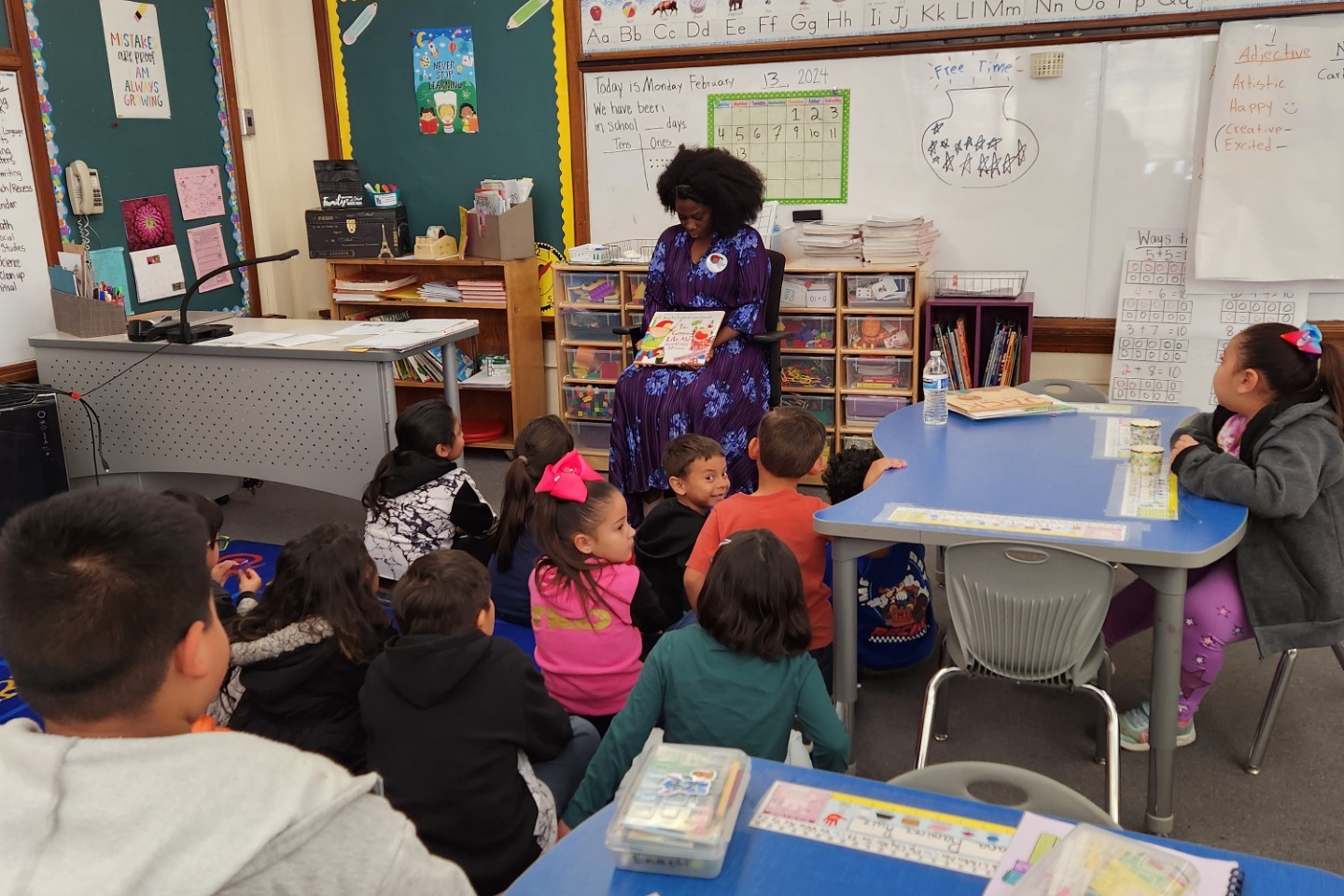 A guest reader holds up a book as she reads to students sitting in front of her